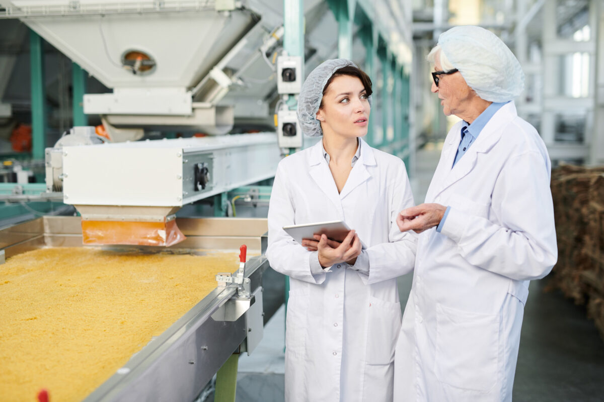 Portrait de deux ouvrières effectuant une inspection de la qualité de la production dans une usine alimentaire, debout près d'un convoyeur et utilisant une tablette numérique, espace de copie